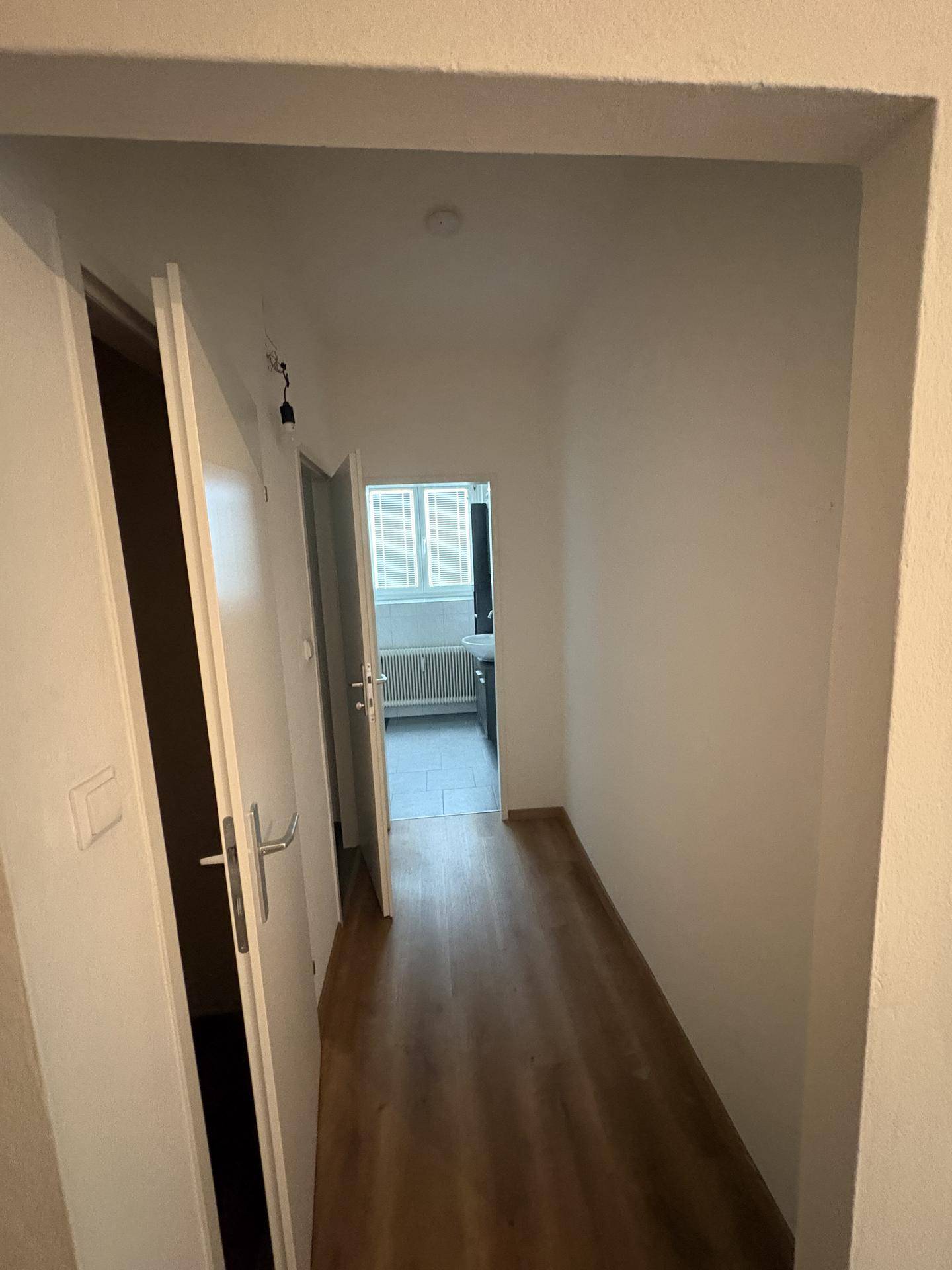 Langer Flur mit Laminatboden und Blick in ein weiteres Zimmer mit Fenster.