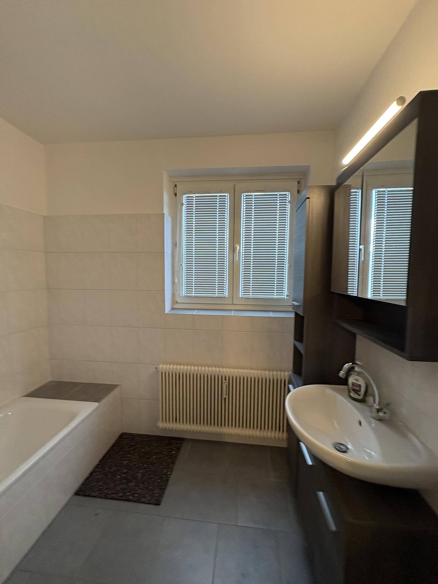 Badezimmer mit Waschbecken, Spiegelschrank, Badewanne und Fenster für Tageslicht.
