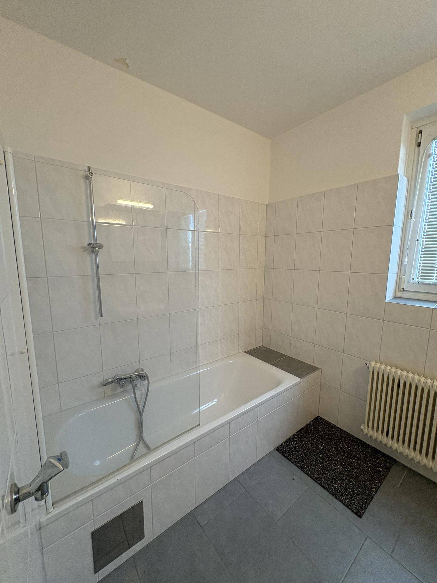 Badezimmer mit Badewanne, weißen Fliesen und einem Fenster für natürliche Belüftung.