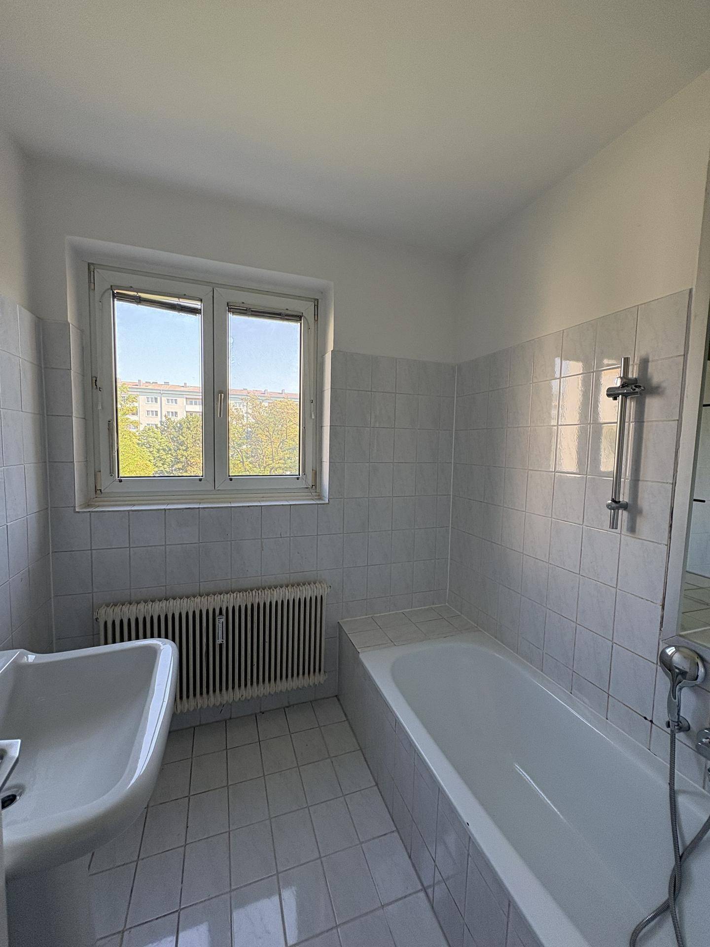 Helles Badezimmer mit weißen Fliesen, Badewanne, Waschbecken und Fenster.