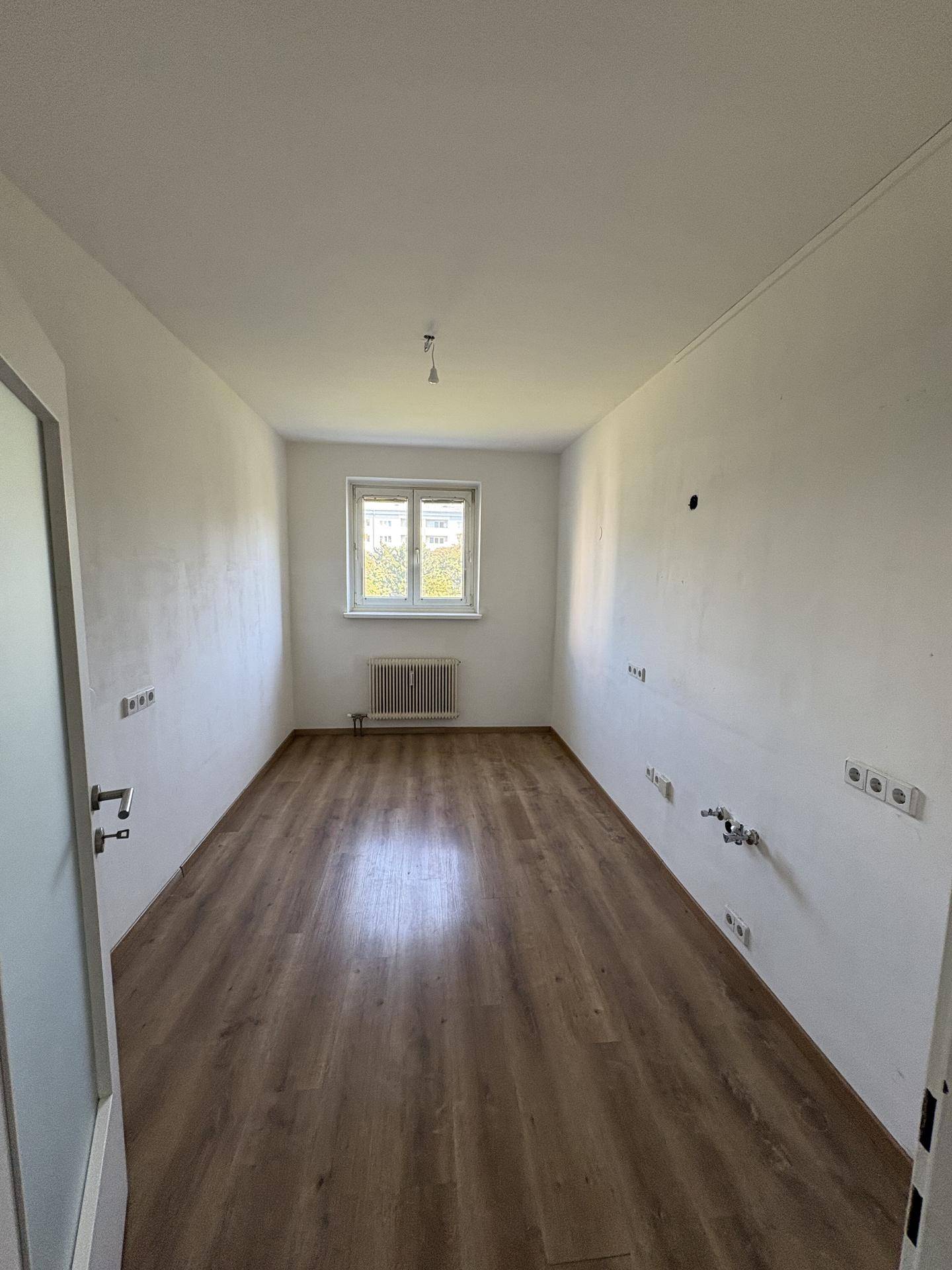 Leerer Raum, vorbereitet für eine Küche, mit Laminatboden und Fenster.