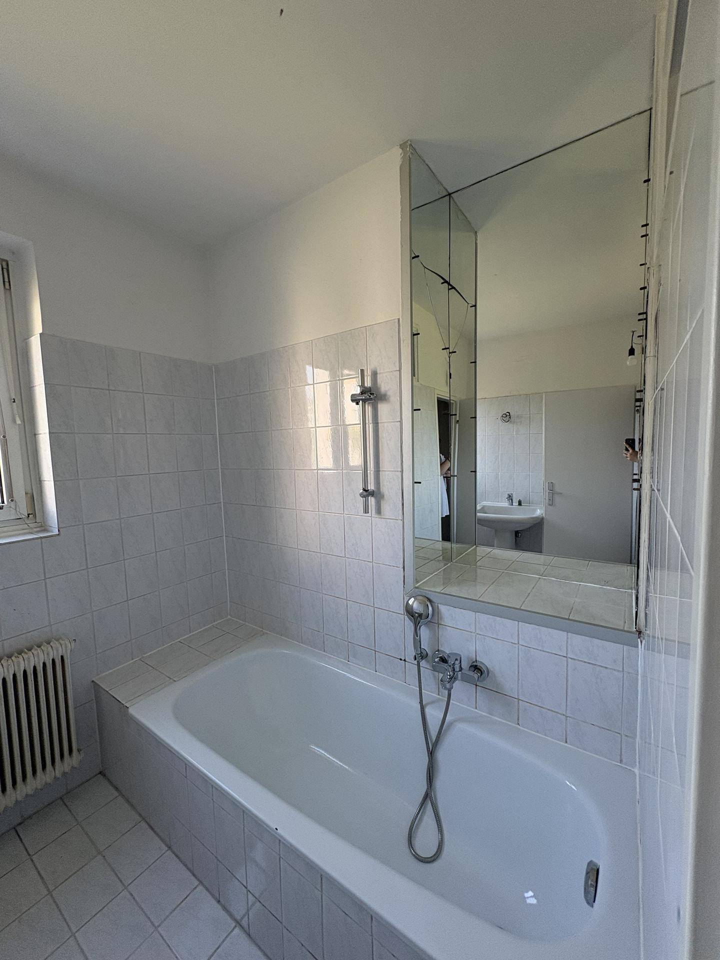 Badezimmer mit Badewanne, weißen Fliesen und großem Spiegel über dem Waschbeckenbereich.