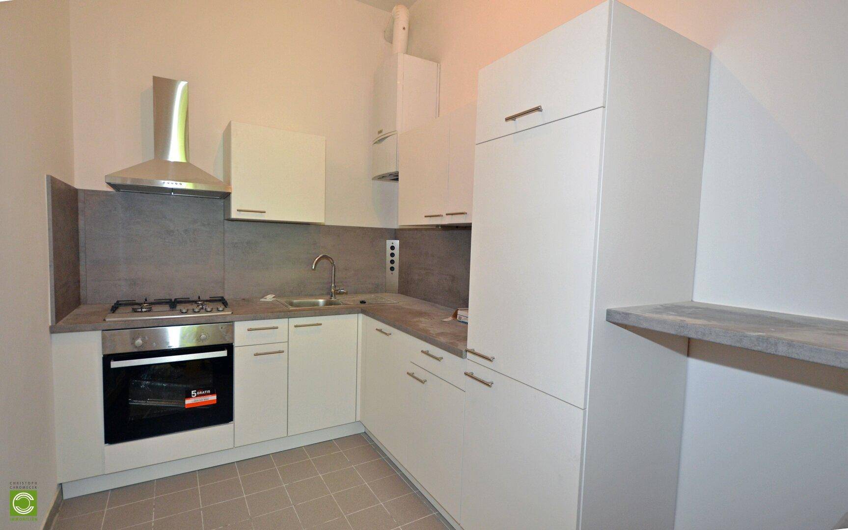 Moderne Küche mit weißen Schränken, Gasherd, Backofen und Dunstabzugshaube.