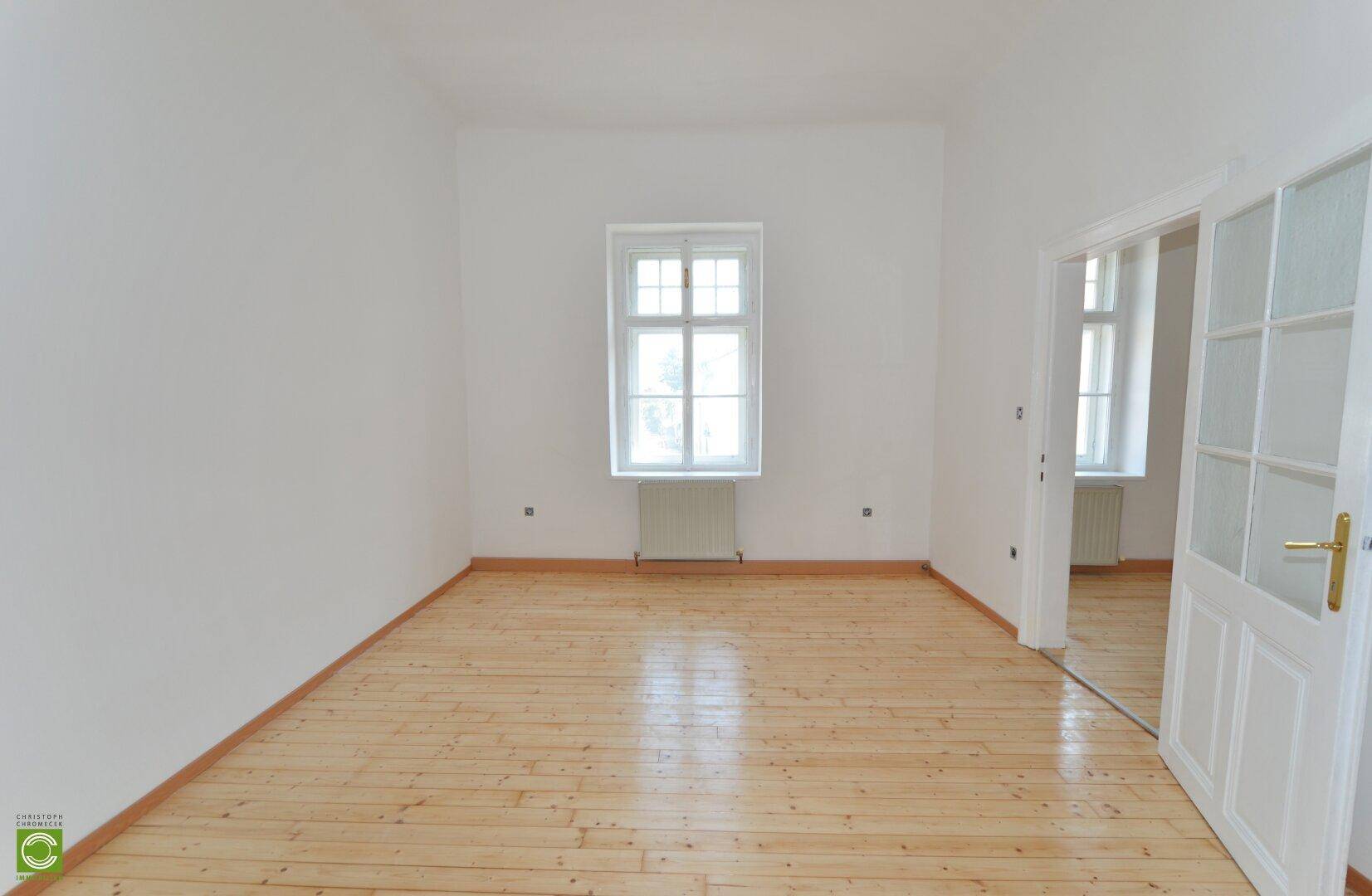 Leerer Raum mit hellen Holzdielen, weiß gestrichenen Wänden und einem großen Fenster.