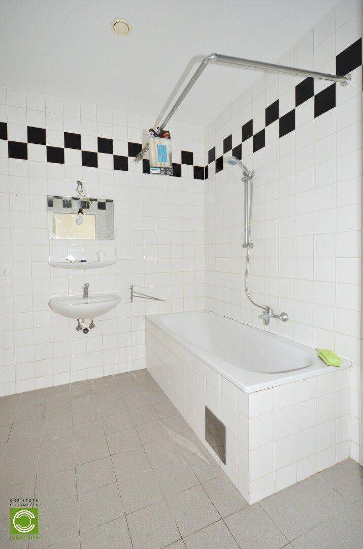 Badezimmer mit Badewanne, Waschbecken und schwarz-weiß gefliestem Dekorband.
