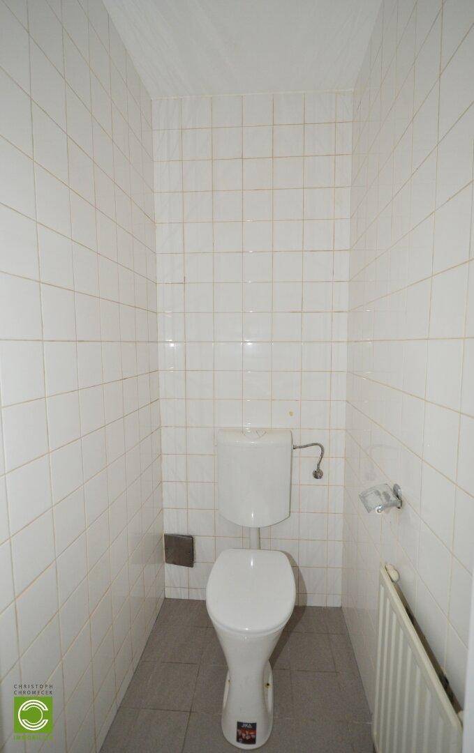 Kleines Gäste-WC mit weißen Wandfliesen, grauen Bodenfliesen und einer Toilette.