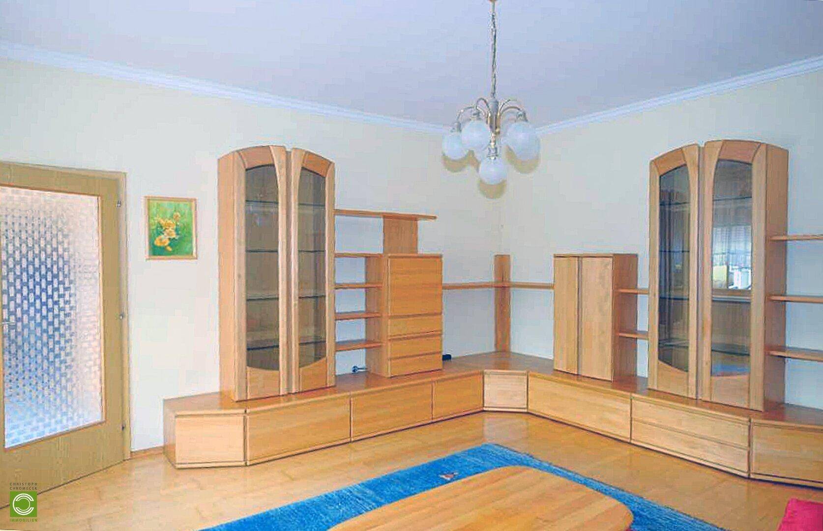 Geräumiges Wohnzimmer mit Holzparkett, heller Einrichtung und einem blauen Teppich als Farbakzent.