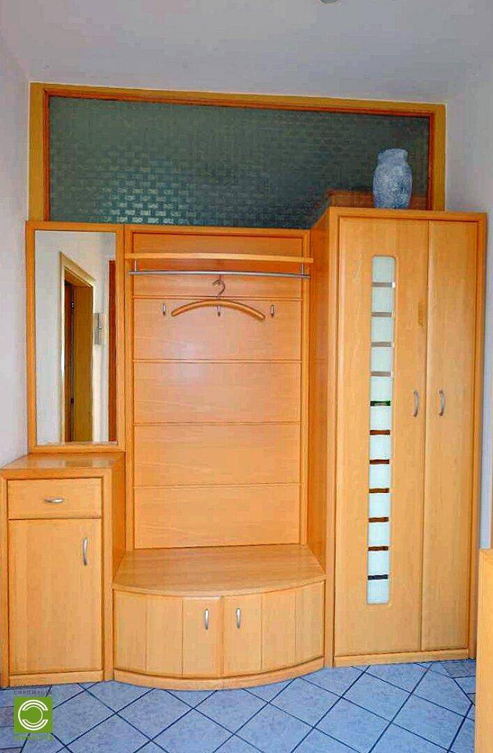 Eingangsbereich mit Garderobe, Spiegel und Holzmöbeln auf gefliestem Boden.