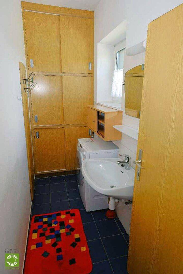 Kleiner Hauswirtschaftsraum mit Waschbecken, Waschmaschine und praktischen Holzschränken.