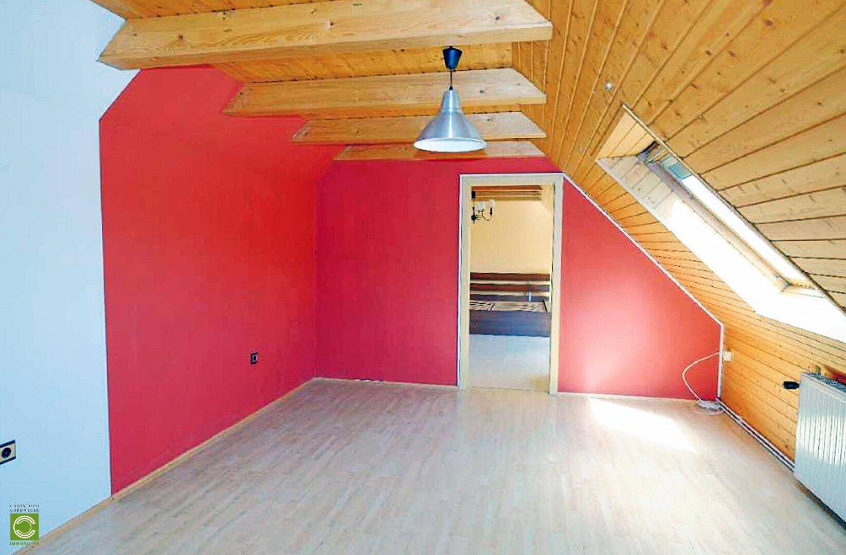 Dachgeschosszimmer mit roten Wänden, Holzverkleidung und Dachfenster, hell und geräumig.