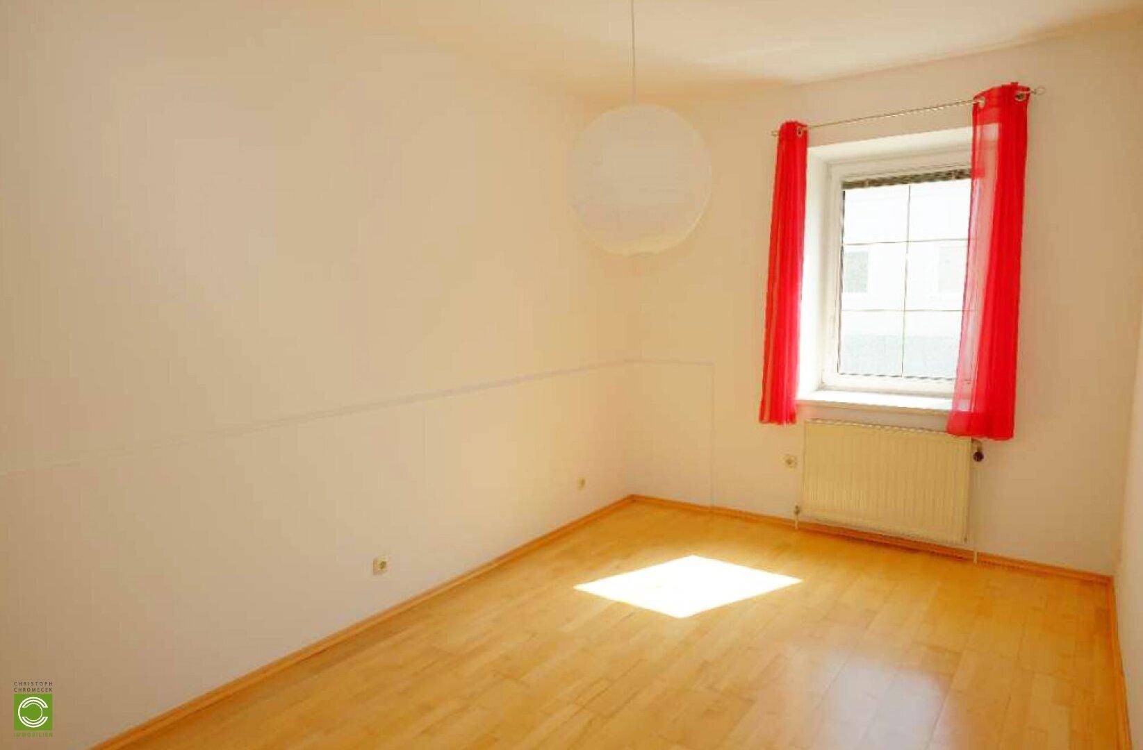 Helles Schlafzimmer mit Holzparkett und einem Fenster, das viel Tageslicht hereinlässt.