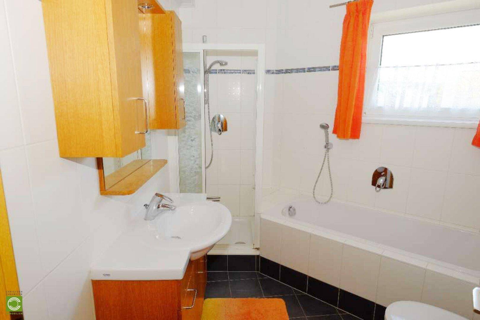Badezimmer mit Badewanne, Dusche und Waschbecken, ausgestattet mit Holzschränken und Fenster.