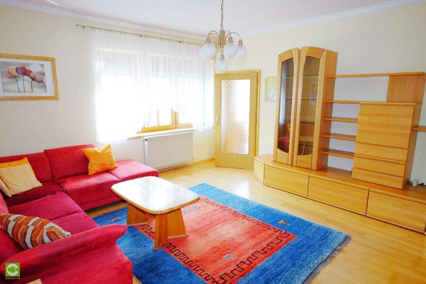 Gemütliches Wohnzimmer mit rotem Sofa, Holzboden und großem Fenster für viel Tageslicht.