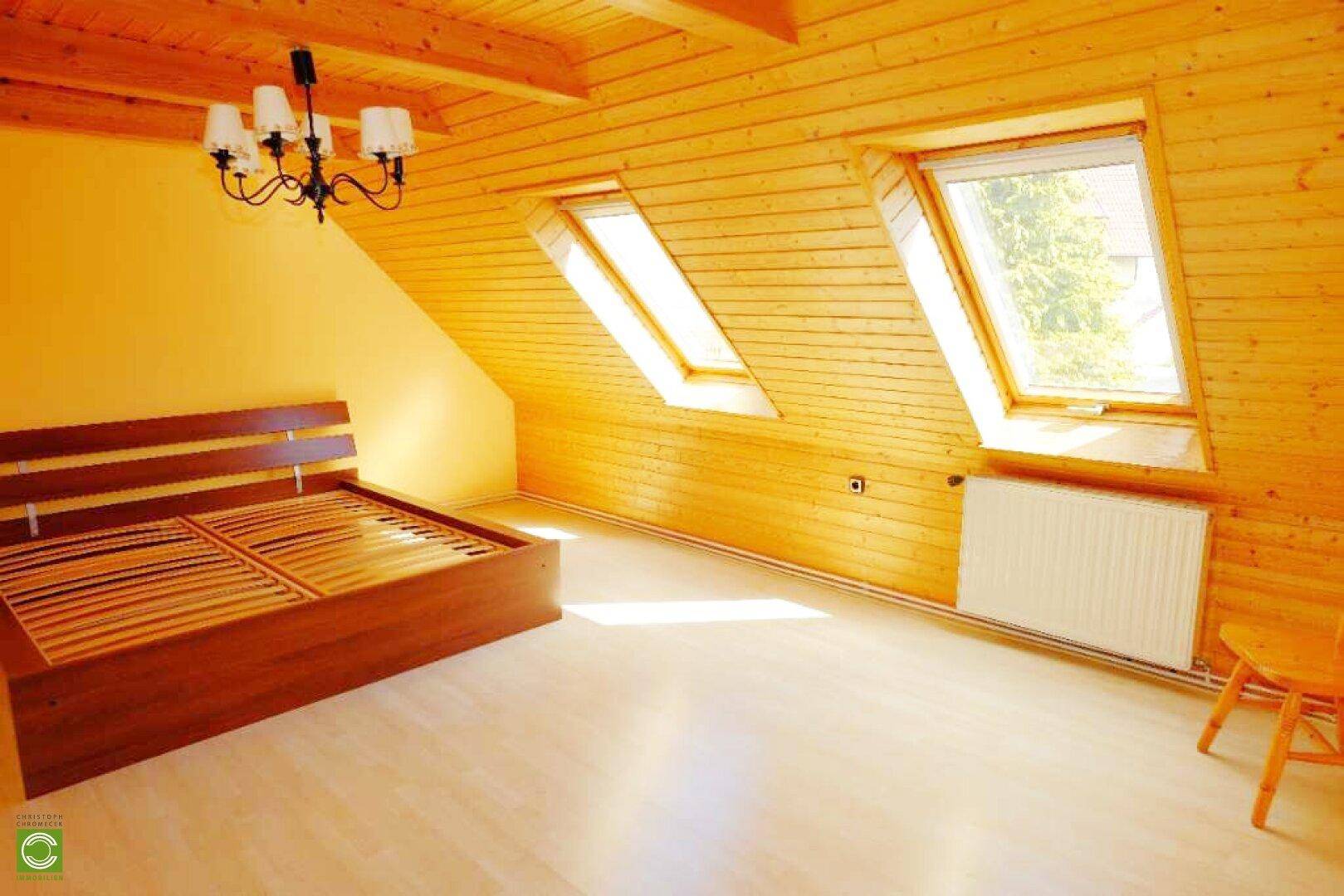 Dachgeschoss-Schlafzimmer mit Holzverkleidung, Dachfenstern und einem Doppelbett, sehr hell.