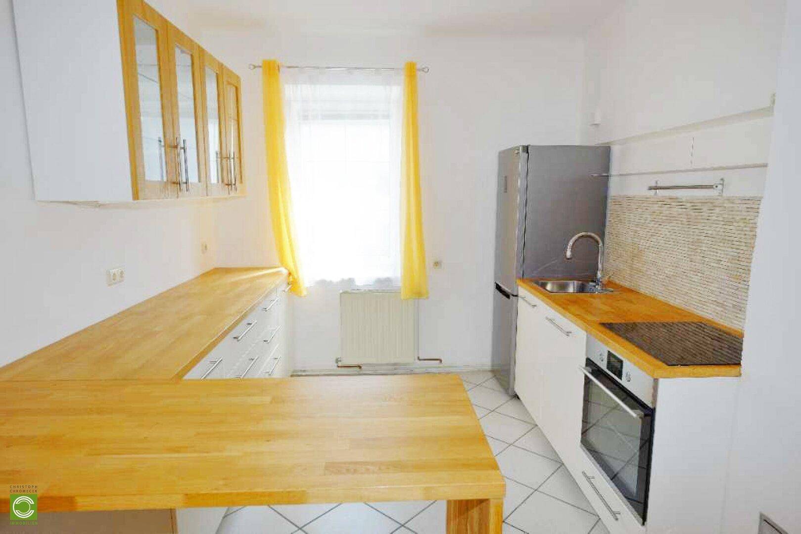 Moderne Küche mit weißen Schränken, Holz-Arbeitsplatten und integrierten Geräten, inklusive Kühlschrank.