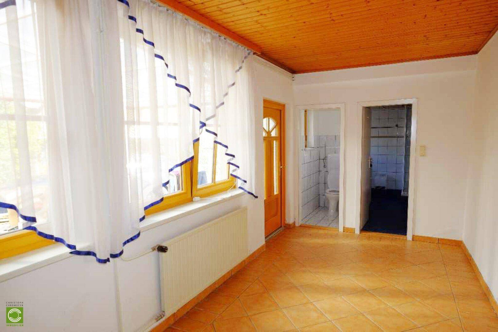 Heller Raum mit Terrakotta-Fliesen und Holzdecke, angrenzend an ein Badezimmer.