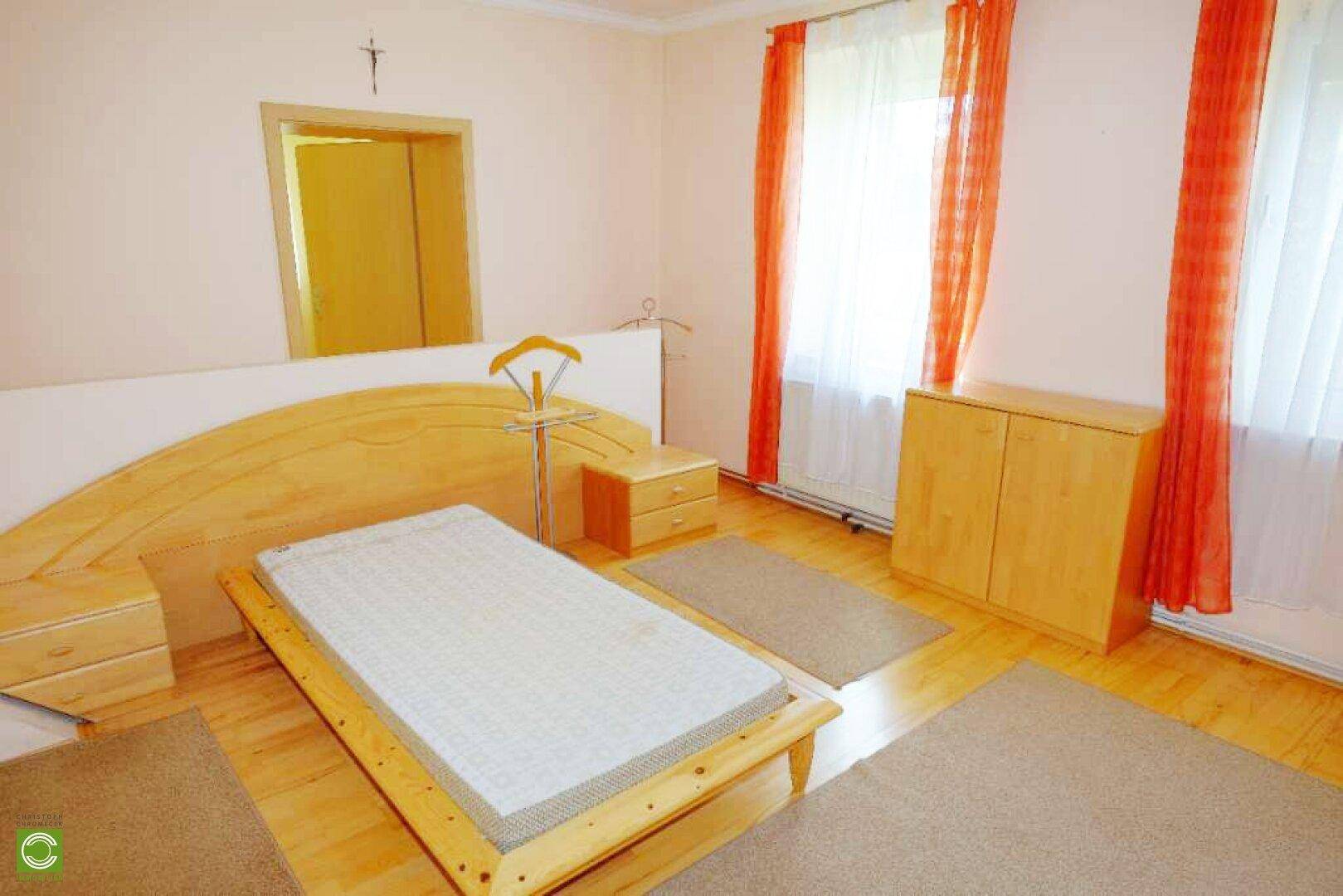 Schlafzimmer mit Holzbett, Nachttischen und hellen Vorhängen, bietet eine ruhige Atmosphäre.