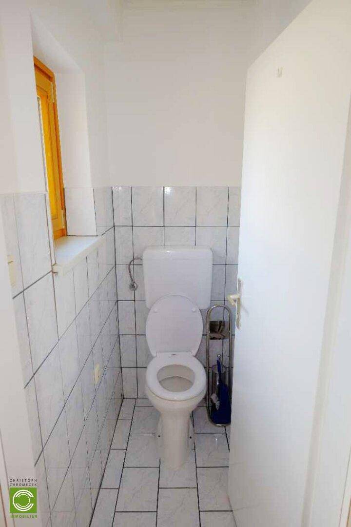 Kleines WC mit Fenster, weißen Fliesen und einfacher Toilette, funktional und hell.