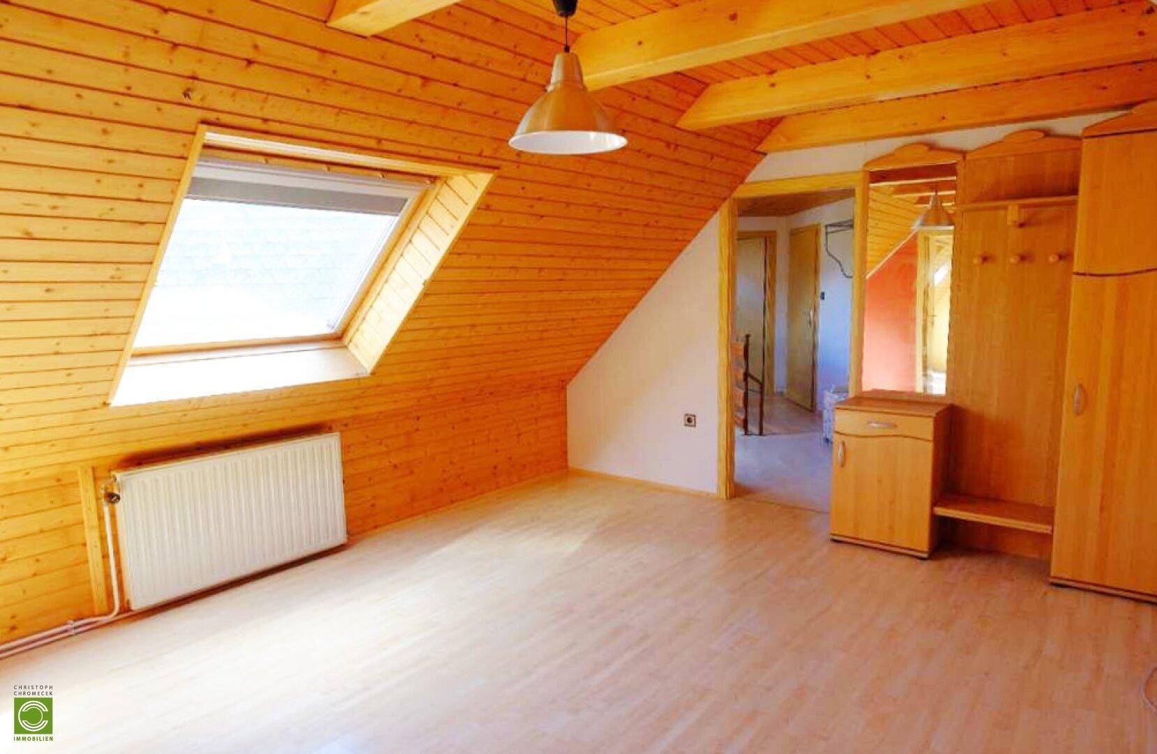 Dachgeschosszimmer mit Holzverkleidung, Dachfenster und Garderobe, hell und geräumig.