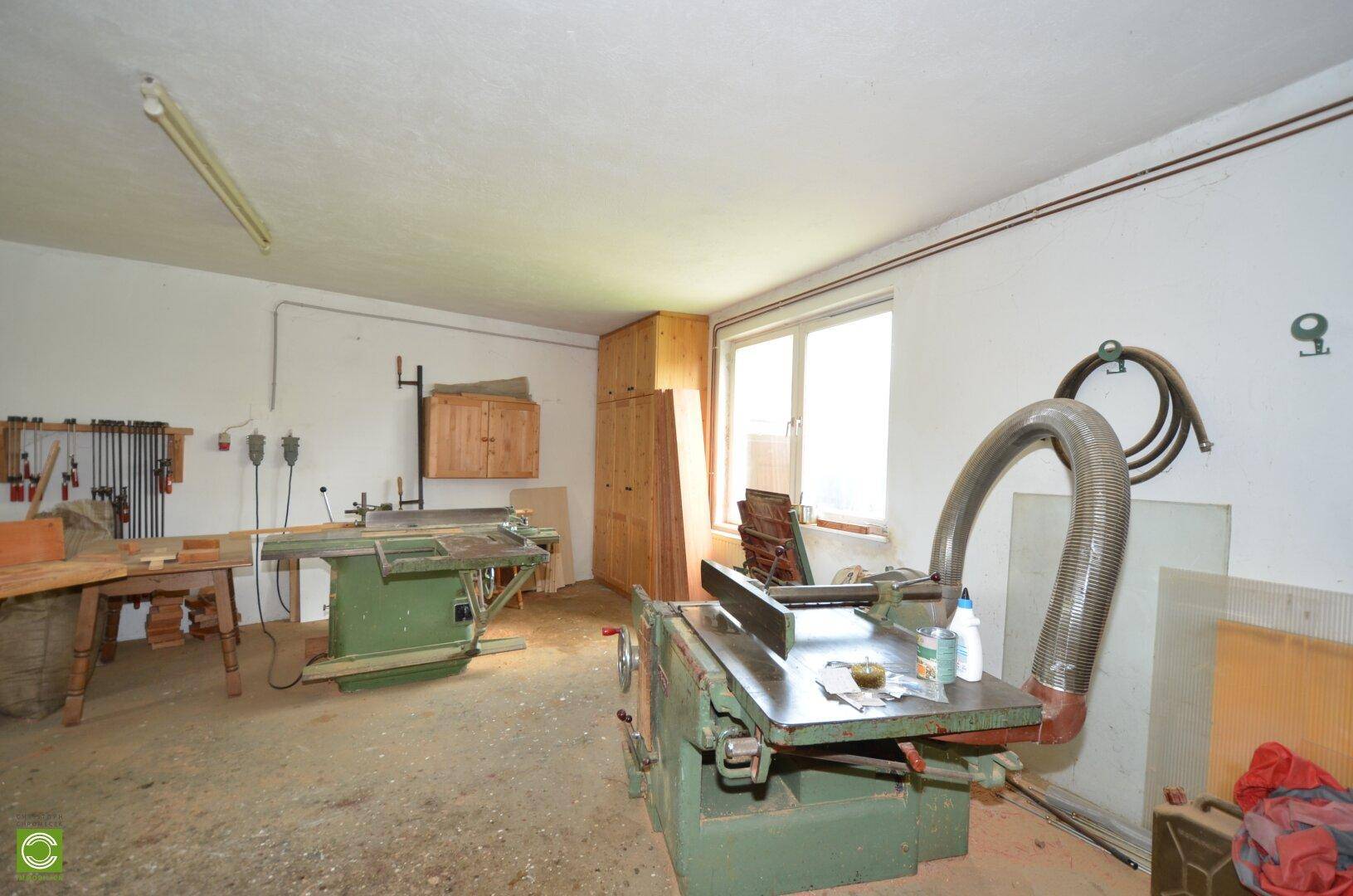 Gut ausgestattete Werkstatt mit verschiedenen Holzbearbeitungsmaschinen und natürlichem Lichteinfall durch ein Fenster.
