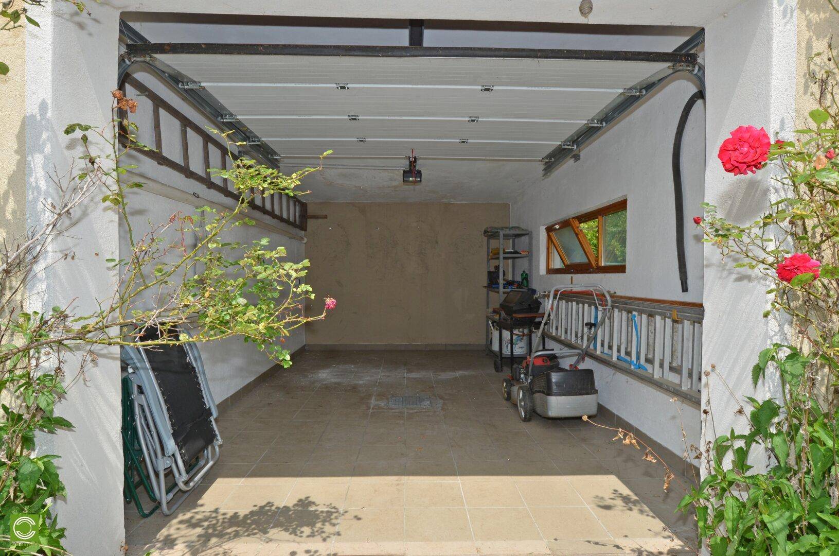 Geräumige Garage mit gefliestem Boden und offenem Tor, umgeben von blühenden Rosenbüschen.