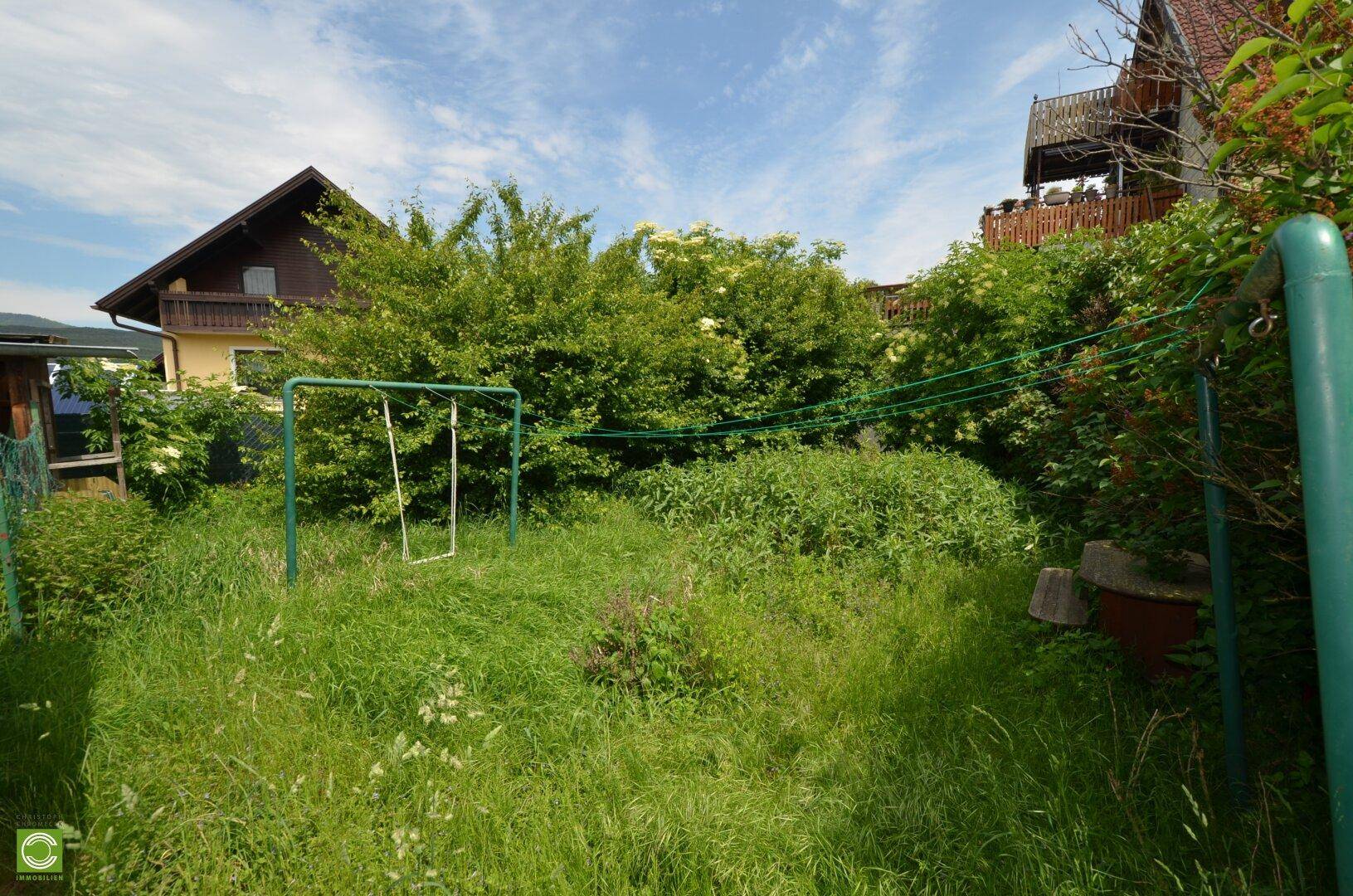Naturbelassener Gartenbereich mit Schaukelgestell und üppiger Vegetation, ideal für Kinder.
