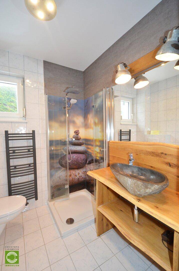 Modernes Badezimmer mit Dusche, Holzwaschtisch und Fenster für Tageslicht.