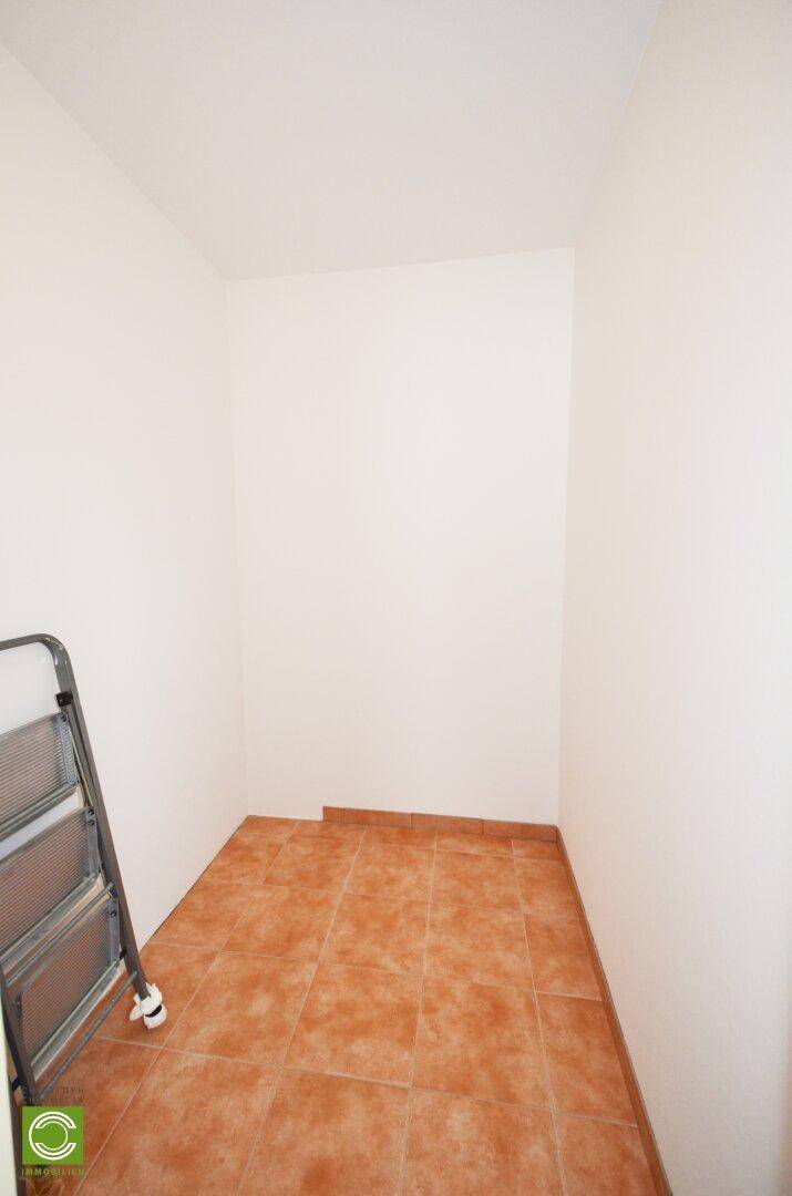 Kleiner Abstellraum mit Terrakottafliesen und weißen Wänden.