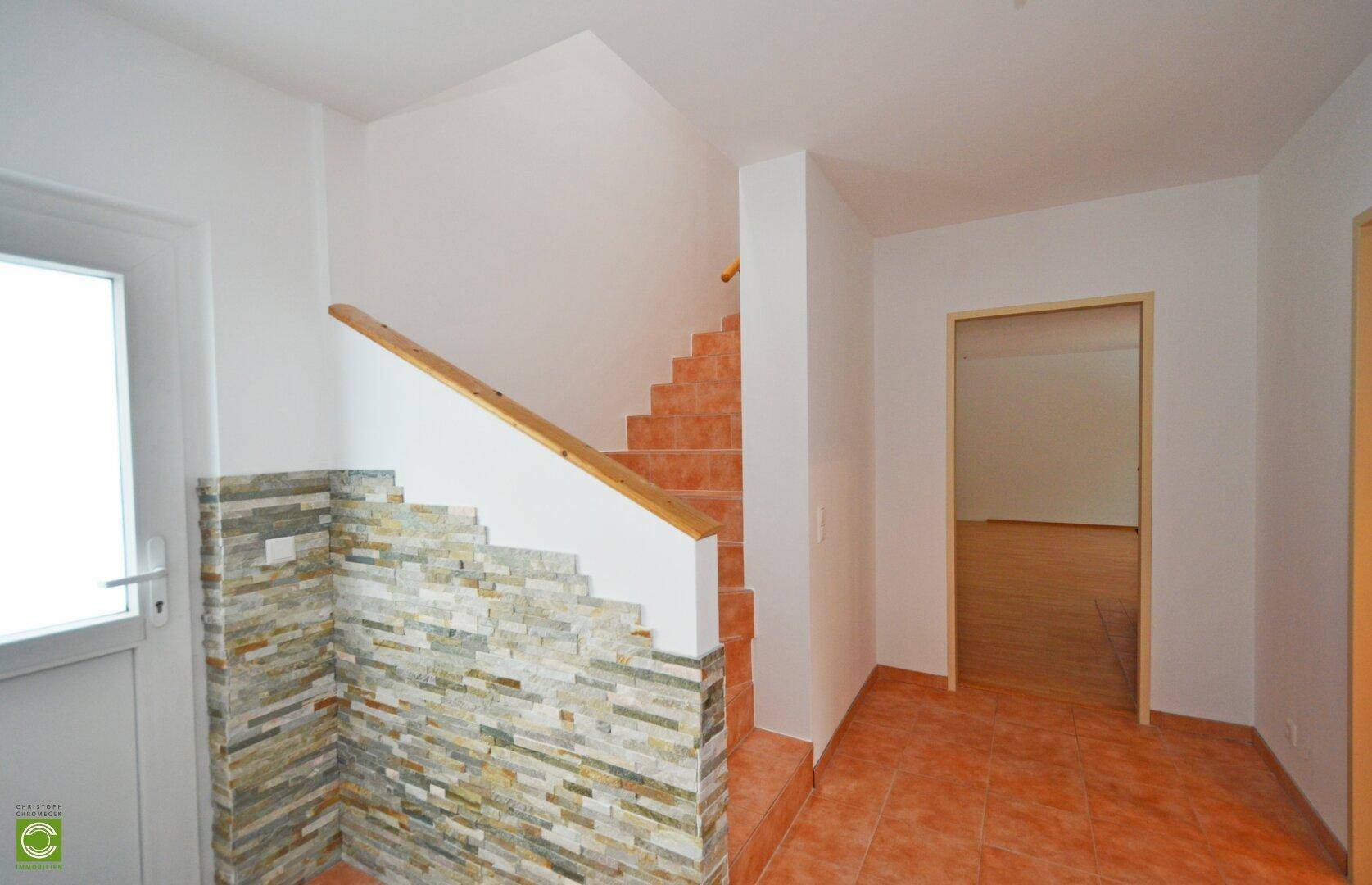 Heller Eingangsbereich mit gefliester Treppe und dekorativer Steinwand.