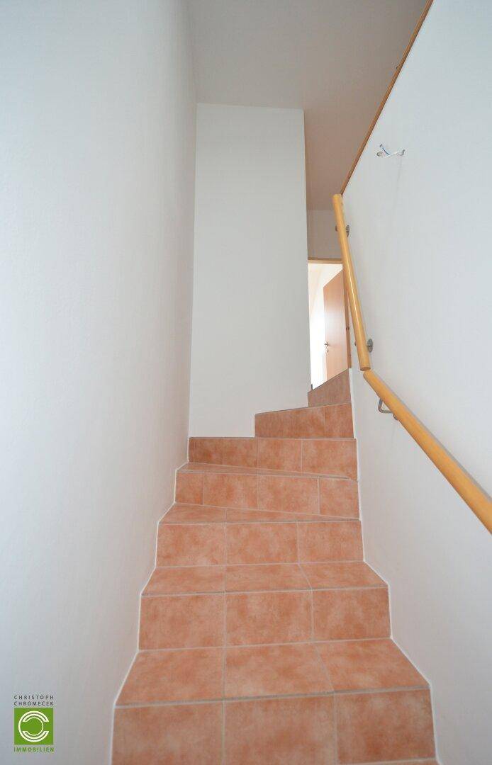 Treppenaufgang mit Terrakottafliesen und Holzgeländer, führt in die obere Etage.