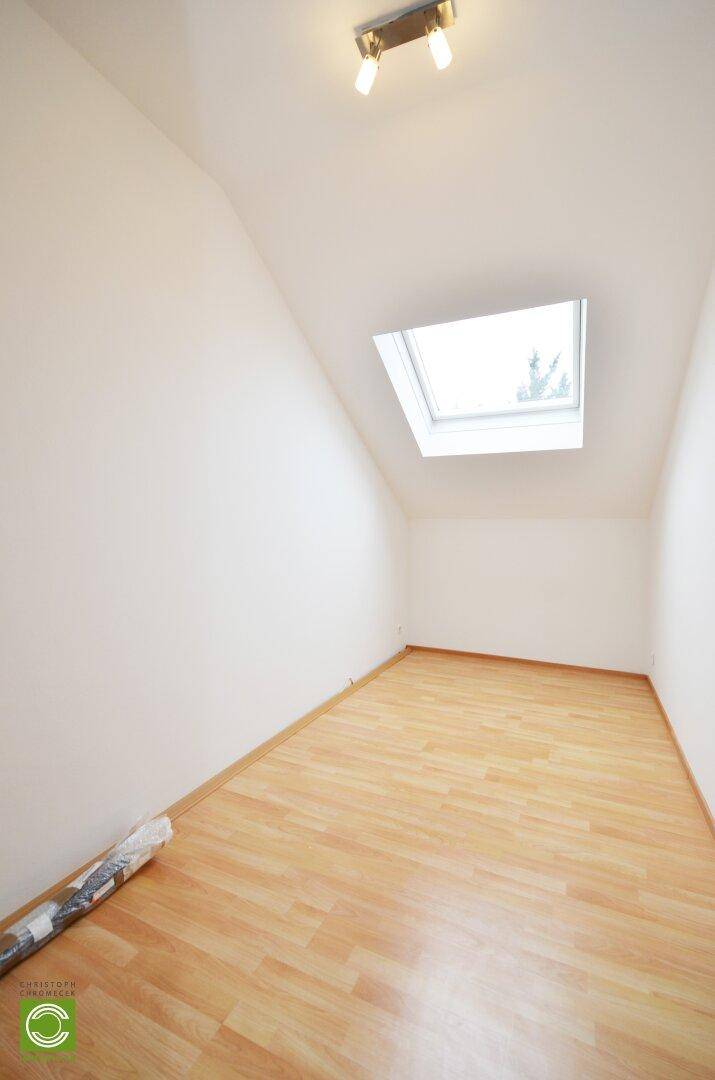 Helles Zimmer im Dachgeschoss mit Schrägdach, Laminatboden und Dachfenster.