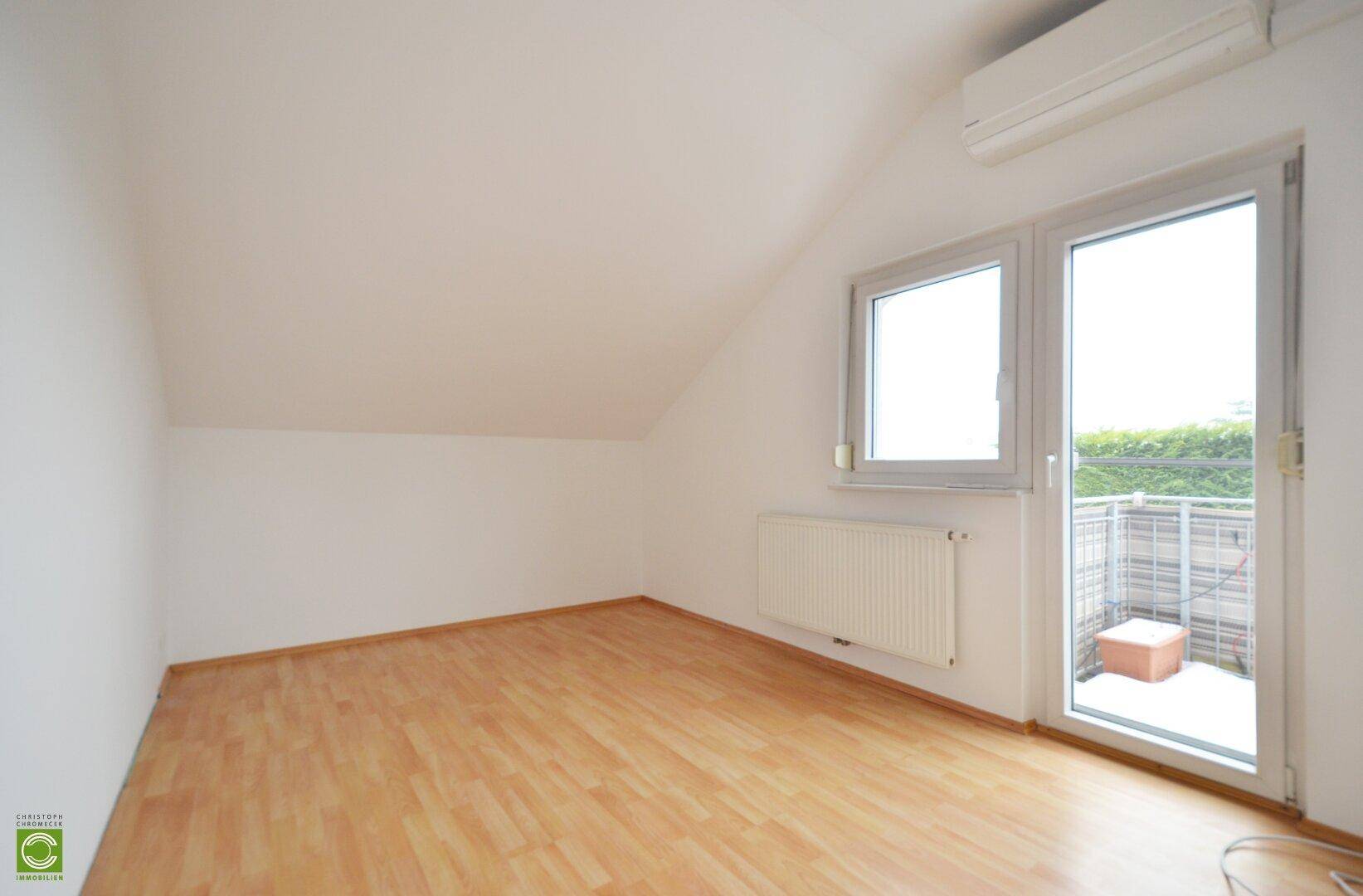 Zimmer im Dachgeschoss mit Laminatboden, Klimaanlage und Balkonzugang.