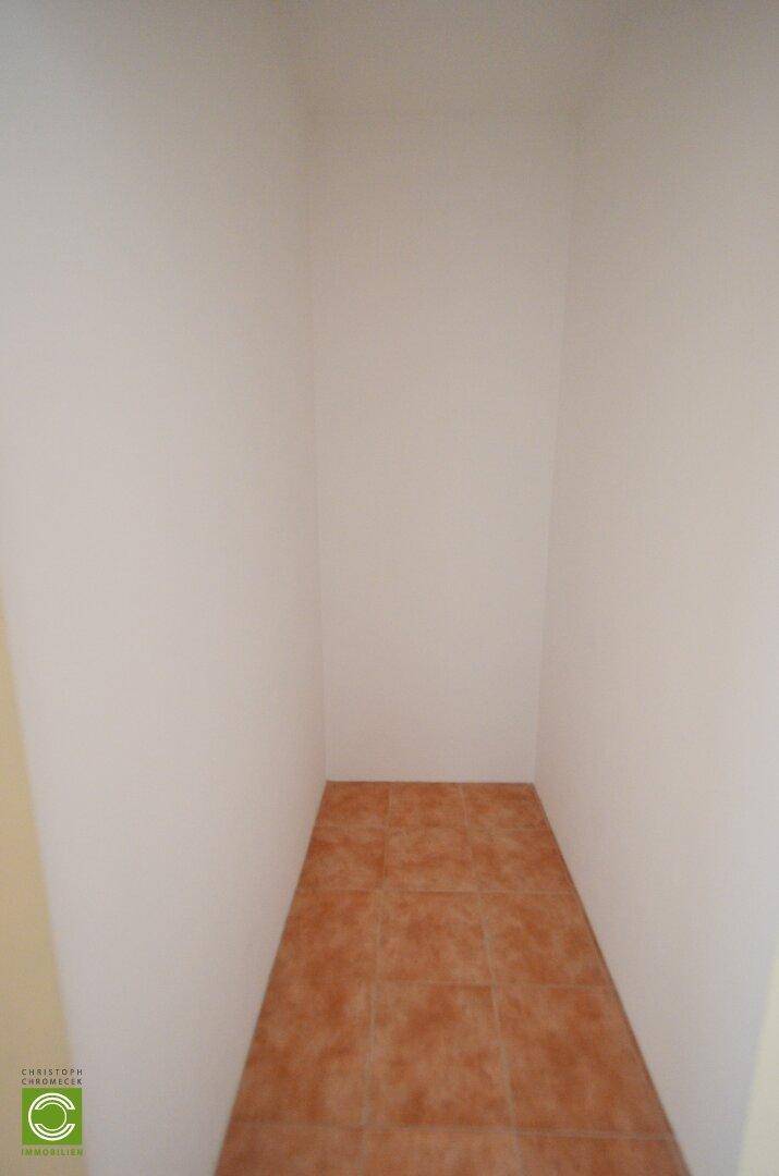 Schmaler Abstellraum mit Terrakottafliesen und weißen Wänden.