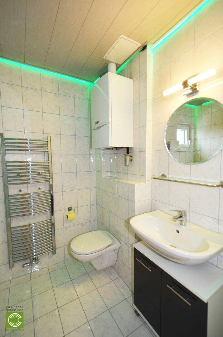 Kleines Badezimmer mit WC, Waschbecken, Heizkörper und Wandheizung.