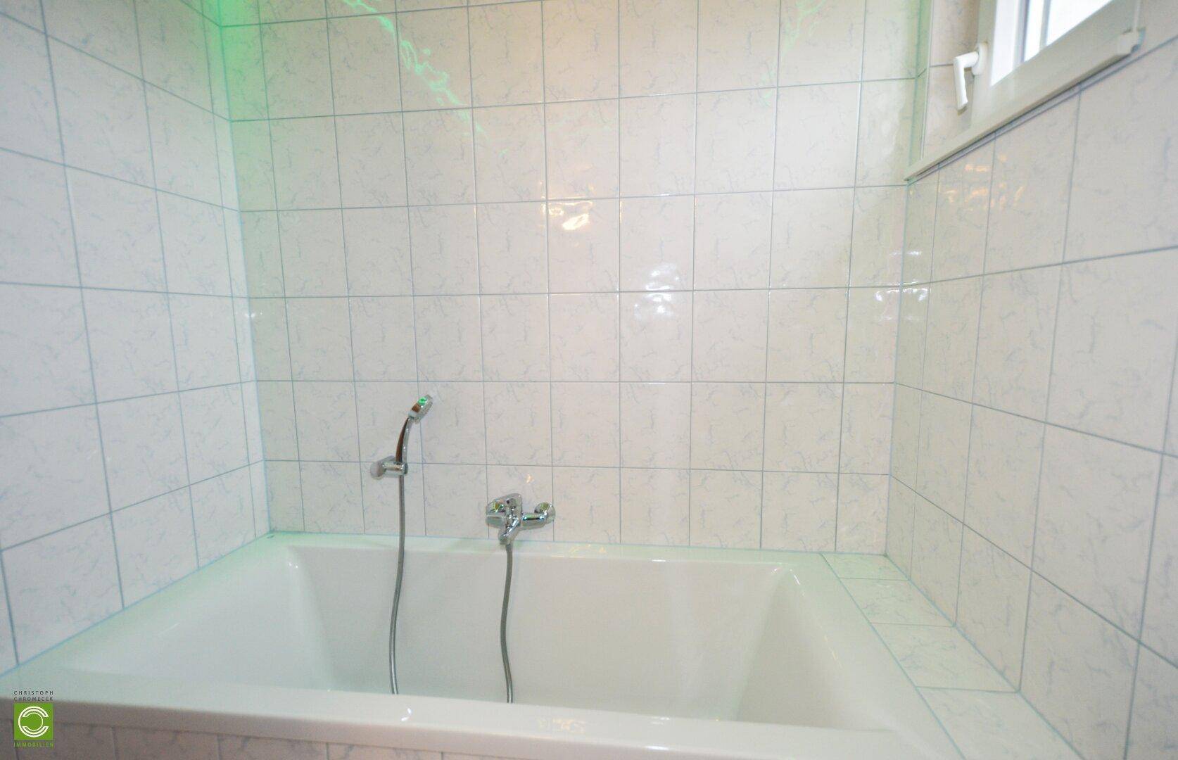 Badezimmer mit eingebauter Badewanne und weißen Fliesen.