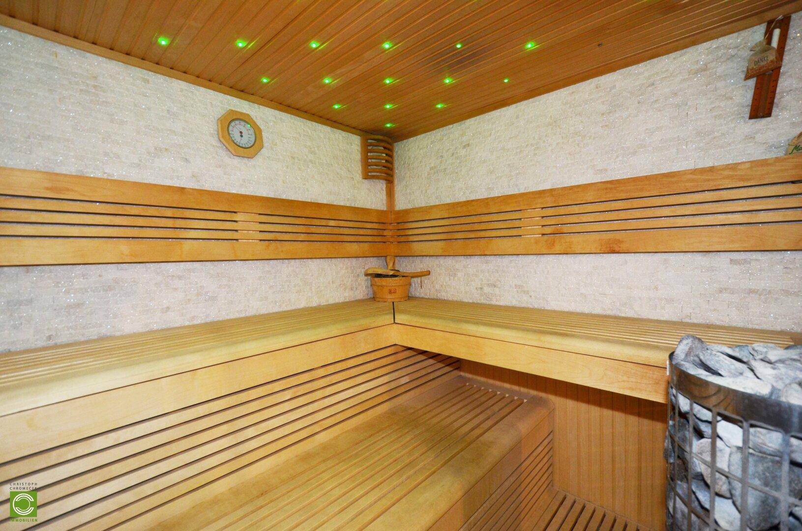 Innenansicht der Sauna mit Holzsitzen, Heizofen und dekorativer Beleuchtung.