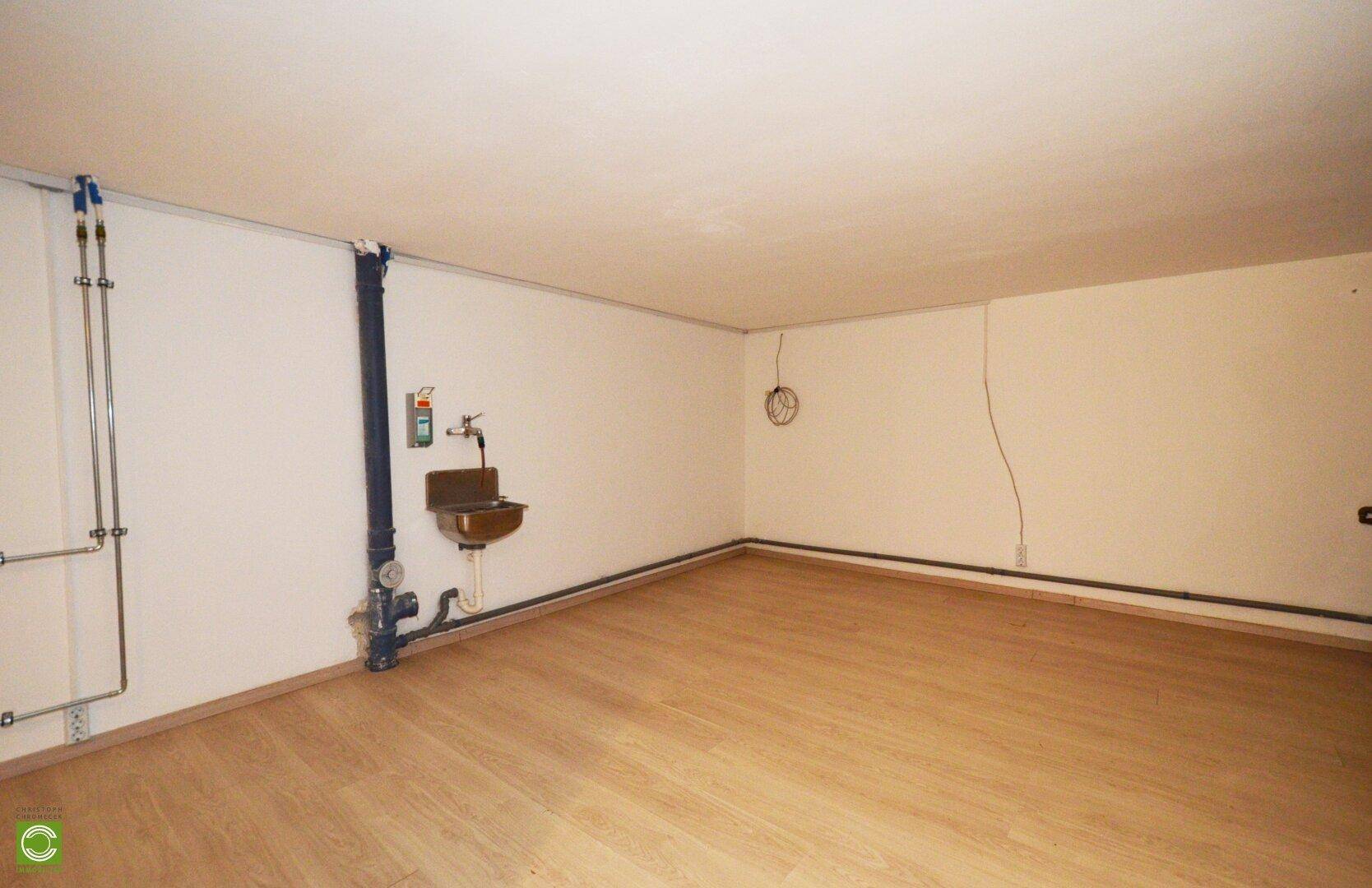 Technikraum im Keller mit sichtbaren Leitungen und Waschbecken.