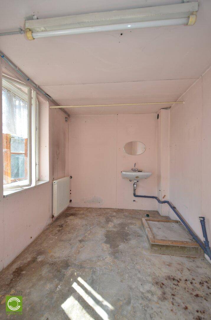 Einfacher Hauswirtschaftsraum mit Waschbecken, Fenster und sichtbaren Rohren.