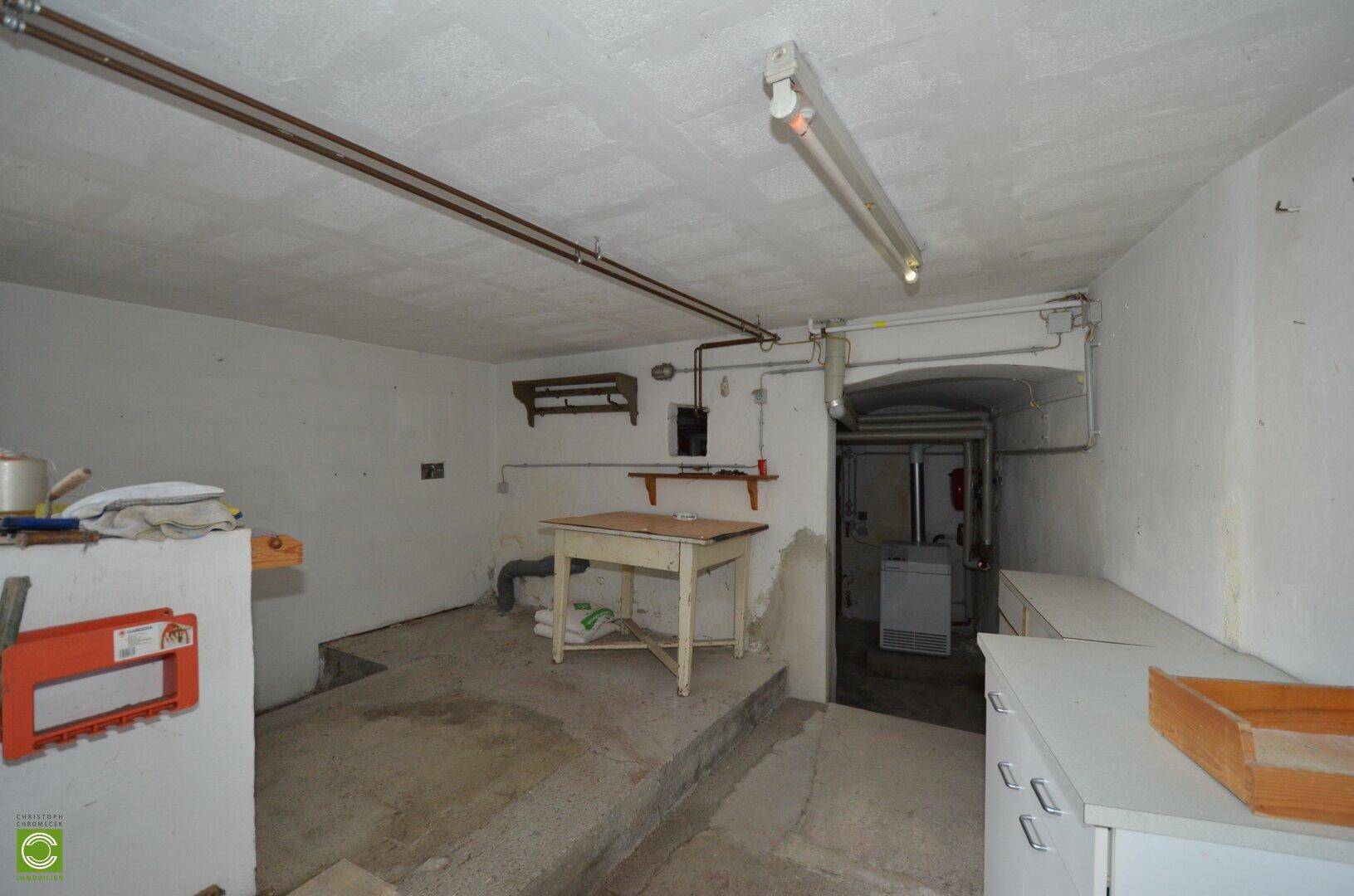 Geräumiger Kellerraum mit Betonboden, Regalen und einem Tisch, ideal als Lagerfläche.