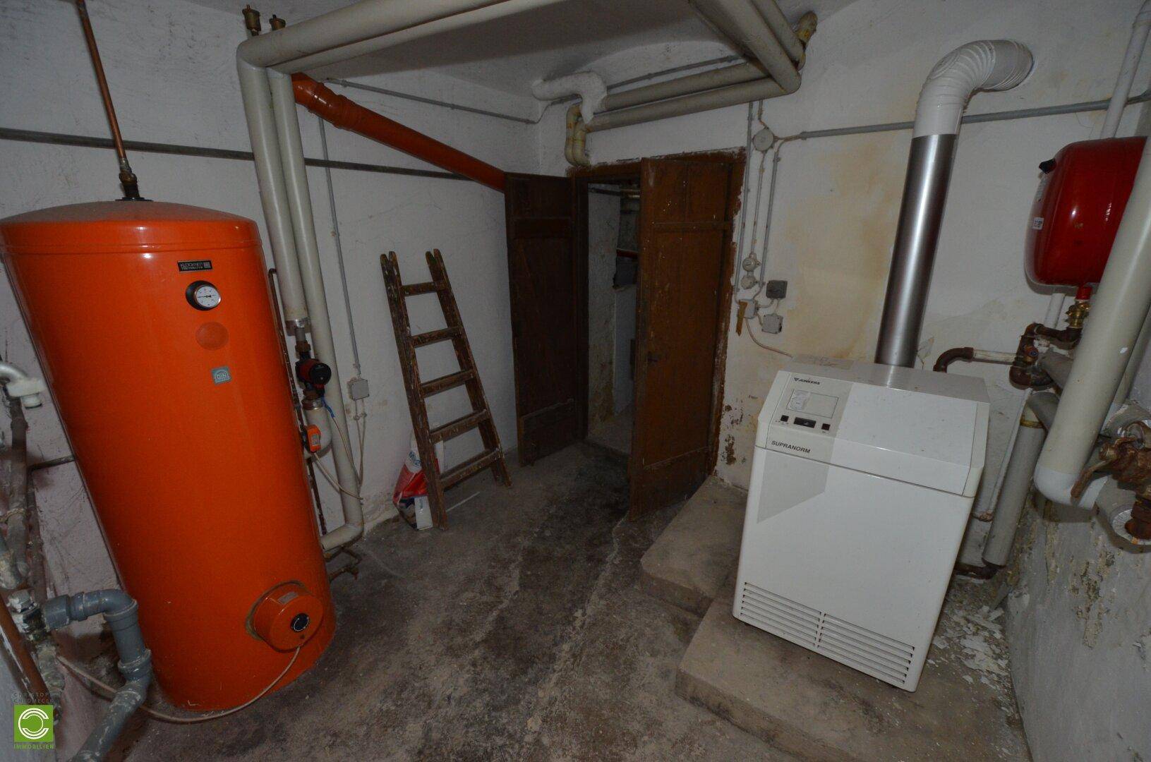 Heizungsraum im Keller mit Warmwasserspeicher und Heizkessel, sichtbare Installationen.