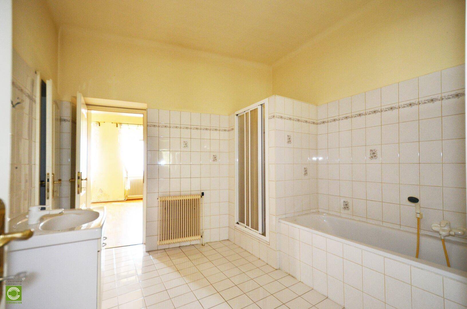 Gefliestes Badezimmer mit Badewanne, Dusche und Doppelwaschbecken, in hellem Zustand.