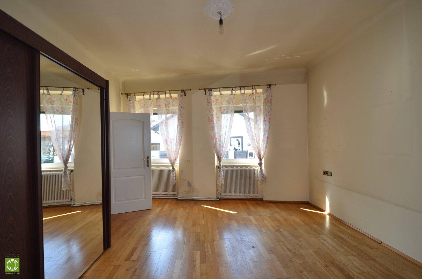 Helles Schlafzimmer mit Parkettboden und zwei Fenstern, inklusive Spiegelschrank.