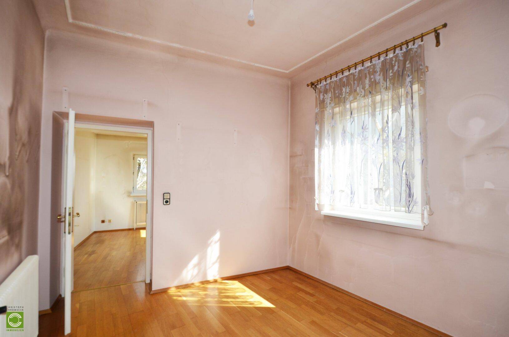 Helles Zimmer mit Parkettboden und einem Fenster, ideal als Schlaf- oder Arbeitszimmer.