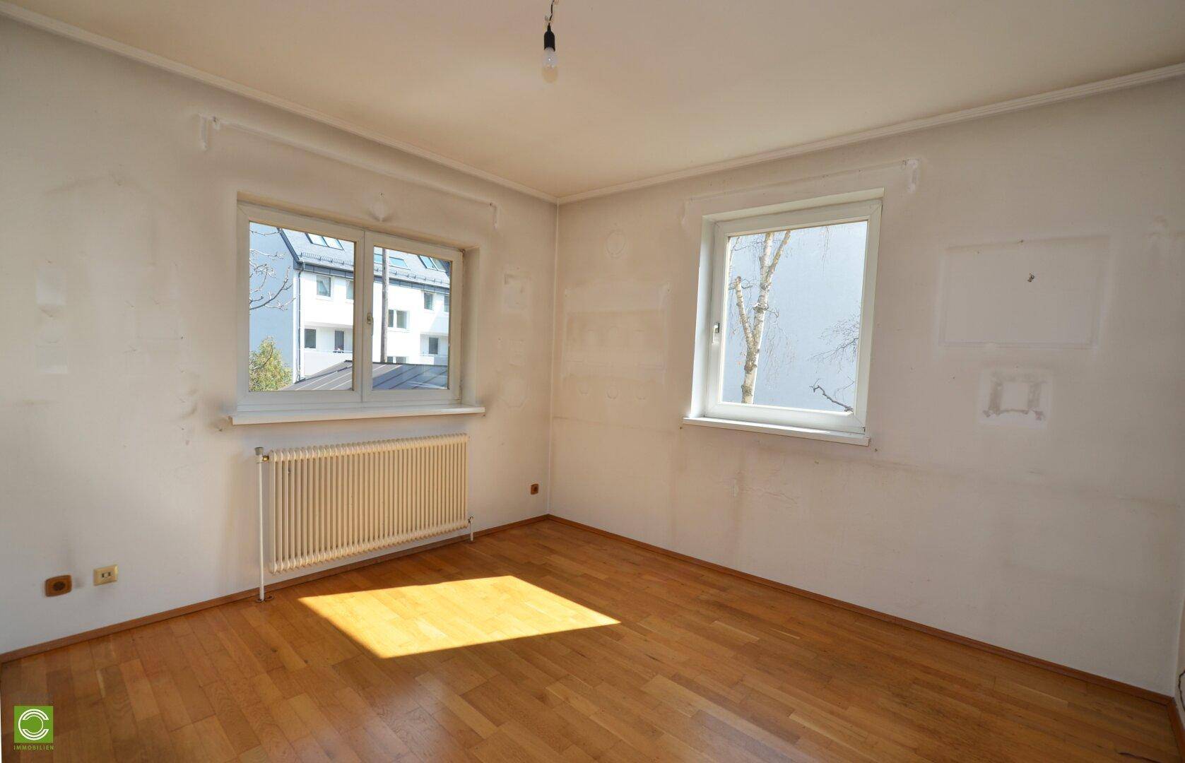 Leeres Zimmer mit Parkettboden und zwei Fenstern, bietet viel natürliches Licht.