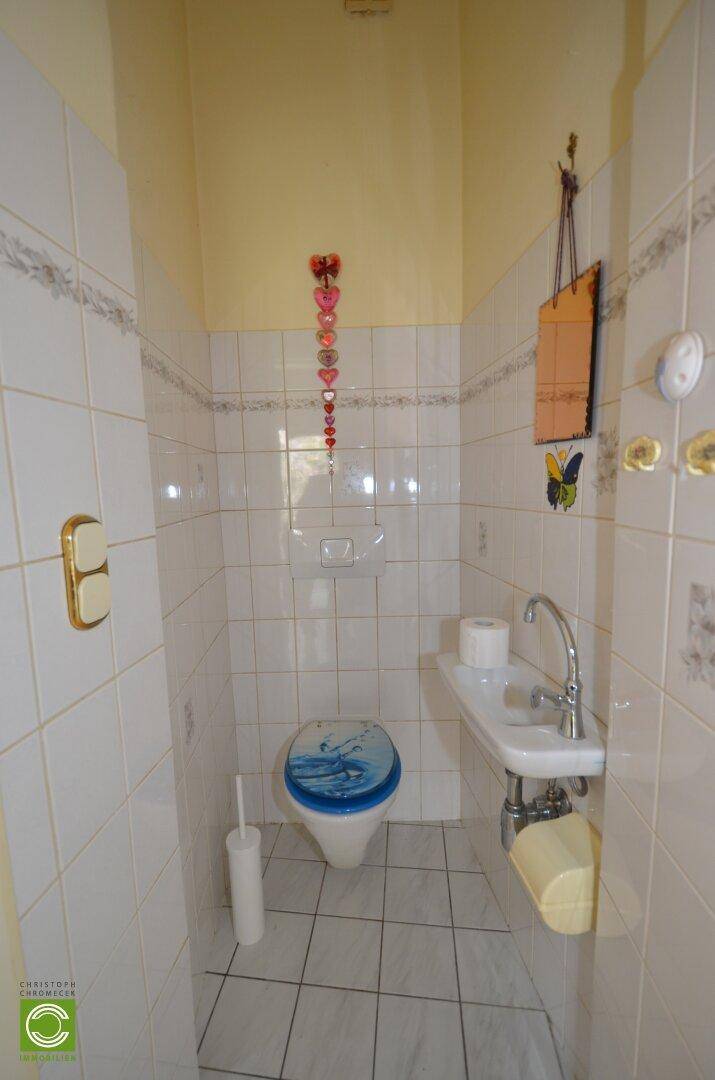Kleines Gäste-WC mit Fliesenboden, Waschbecken und Wand-WC, einfach eingerichtet.