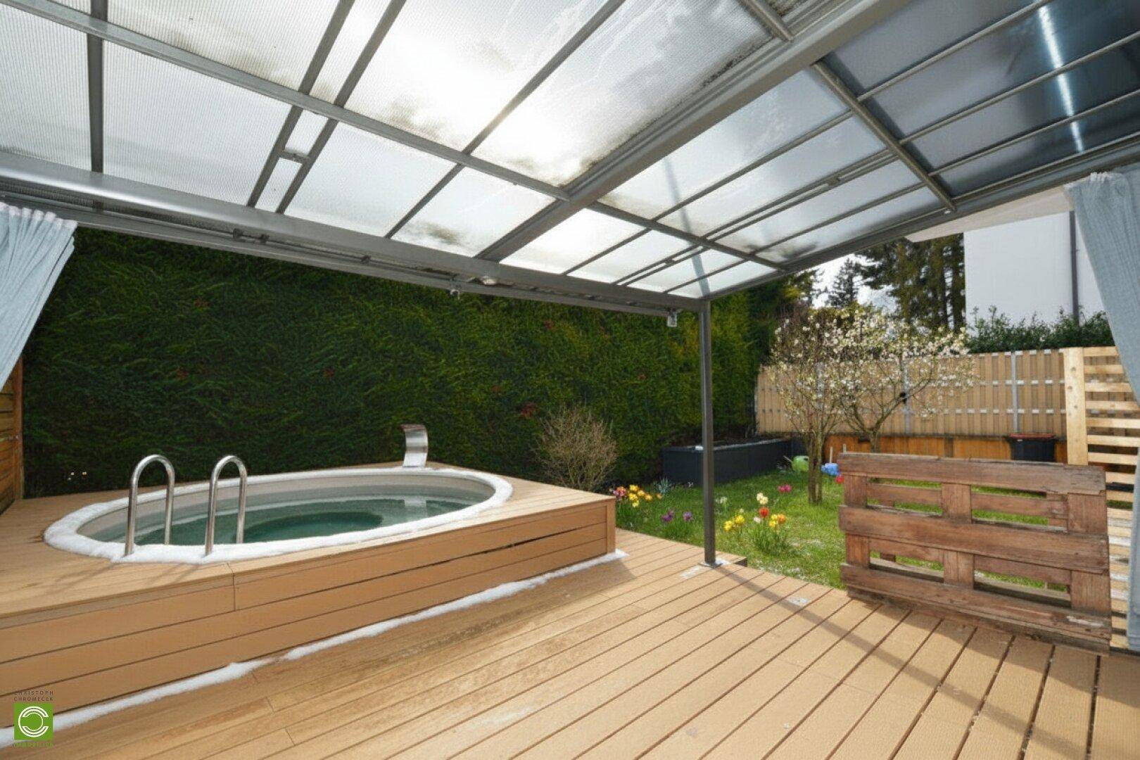 Moderner Terrassenbereich mit Holzdeck, überdachtem Whirlpool und Blick in den blühenden Garten.