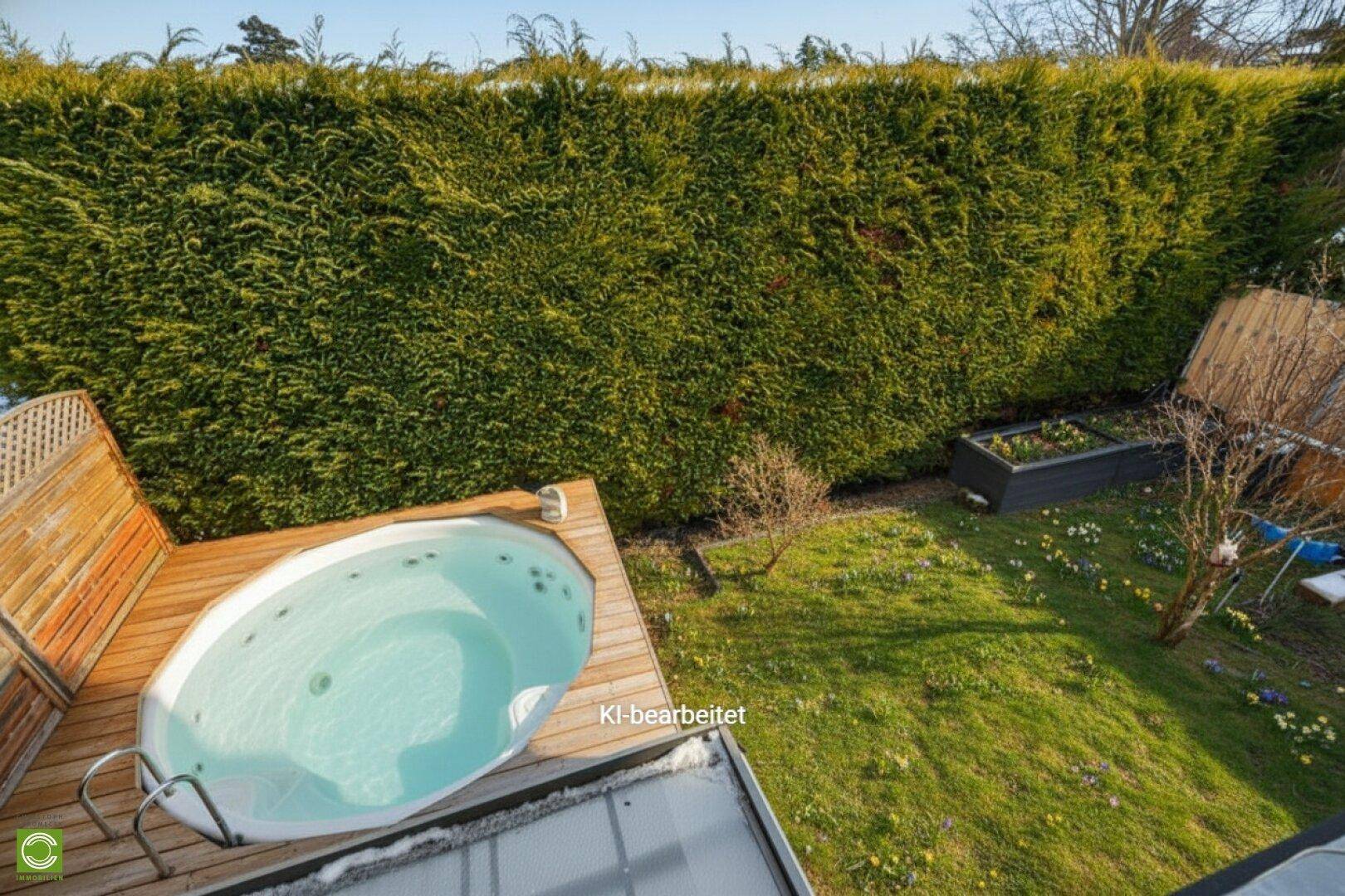 Vogelperspektive des Gartens mit Whirlpool auf Holzdeck und hoher, gepflegter grüner Hecke.