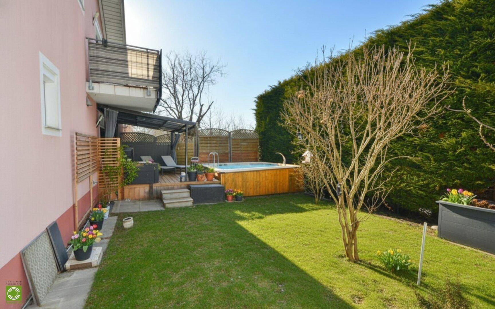Gepflegter Gartenbereich mit Rasen, hoher Hecke und einem Holzdeck mit Whirlpool und Sitzgelegenheiten.