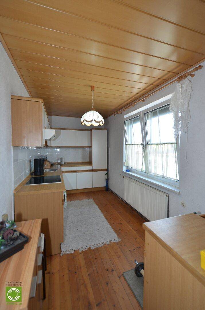 Helle Küche mit Holzdecke, Holzboden und weißen Einbauschränken, ausgestattet mit einem Fenster.
