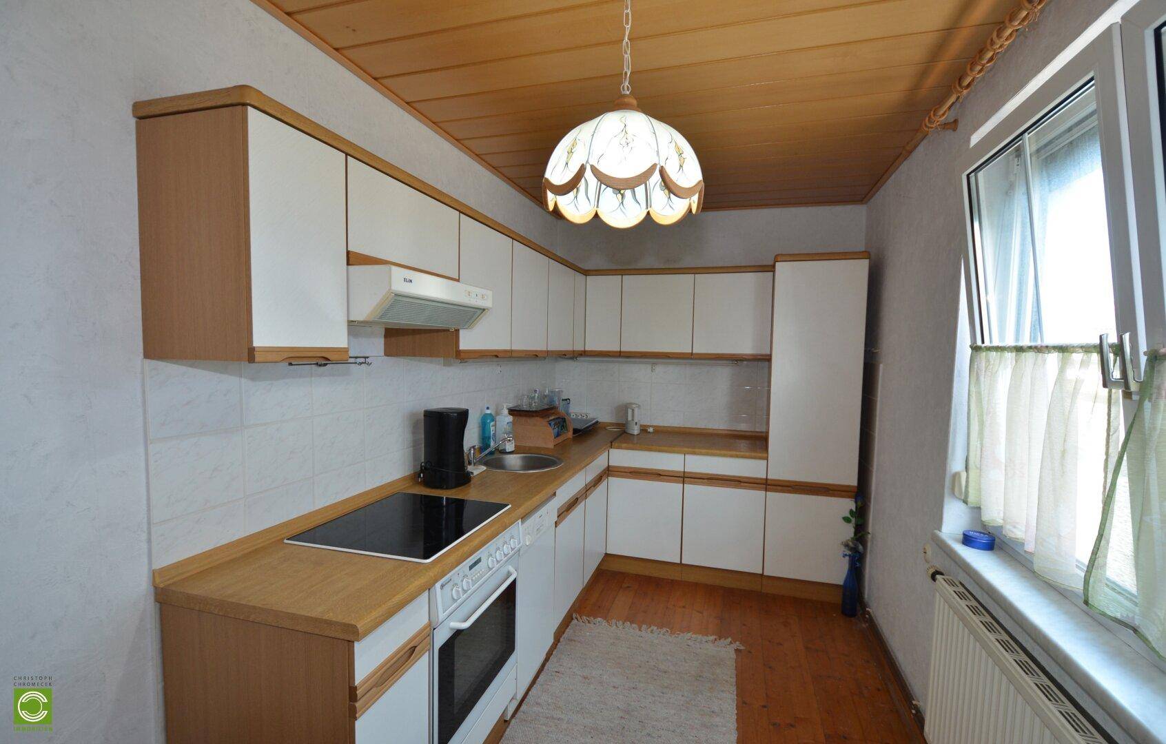 Funktionale Küche mit weißen Schränken, Holzdecke und integriertem Kochfeld und Backofen.